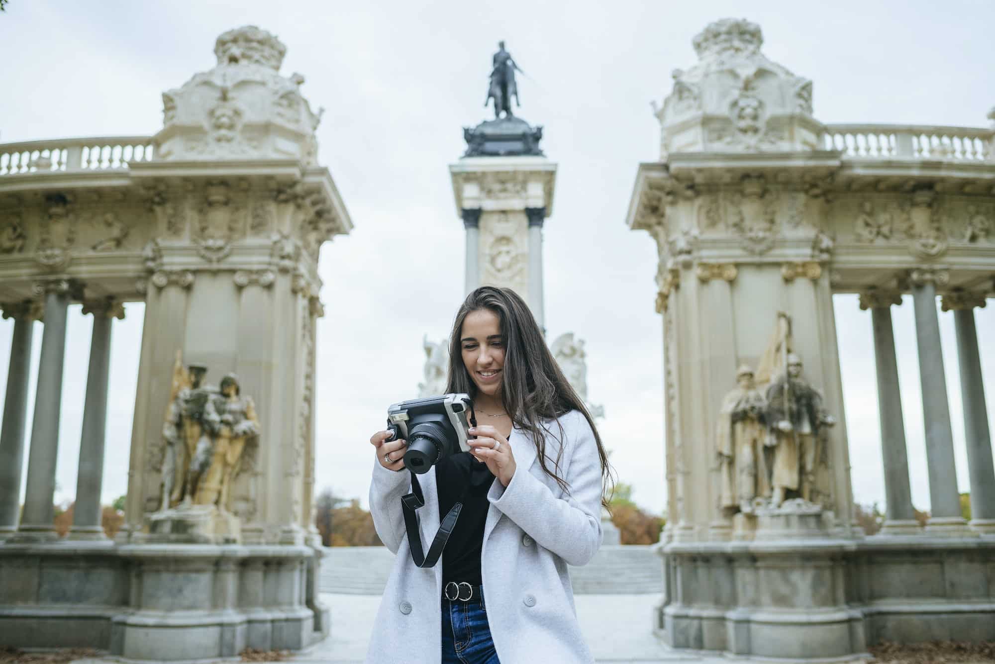 Smiling woman with a camera standing in front of Alfonso XII monument in El Retiro park, Madrid, Spa